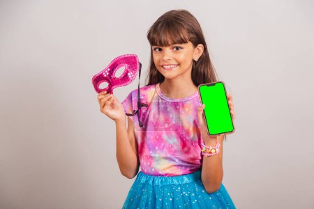 Téléchargez les photos : Belle fille brésilienne, enfant, habillée pour le carnaval au Brésil. tenant smartphone avec écran Chroma vert. - en image libre de droit