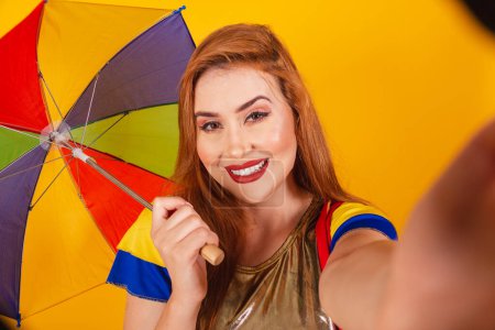 Téléchargez les photos : Rousse brésilienne, avec des vêtements de carnaval, frevo, et parasol coloré. prendre selfie. - en image libre de droit