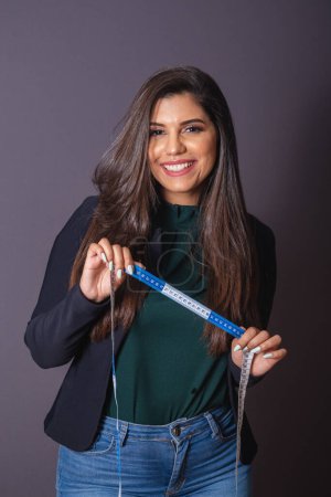 Photo for Horizontal photo. Beautiful Brazilian woman in casual clothes, black blazer jeans. holding measuring tape, nutritionist. - Royalty Free Image