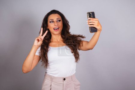 Photo for Beautiful brazilian woman holding smartphone, doing self portrait. Selfie. - Royalty Free Image