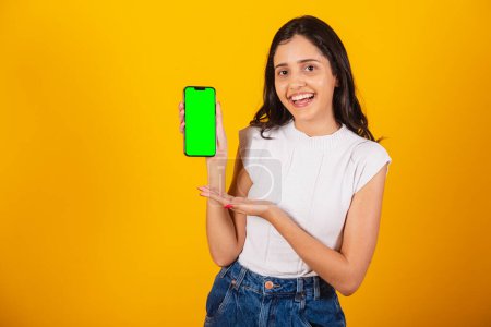 Photo for Beautiful brazilian woman holding smartphone, showing green chroma screen. - Royalty Free Image