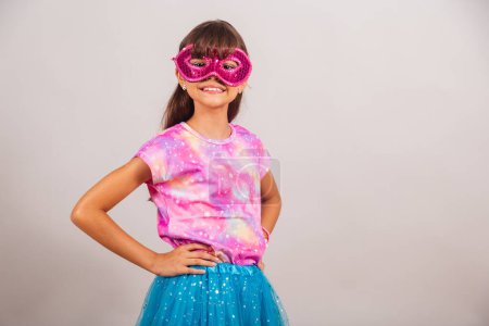 Téléchargez les photos : Belle fille brésilienne, enfant, habillée pour le carnaval au Brésil. avec masque de carnaval, mains sur la taille. - en image libre de droit