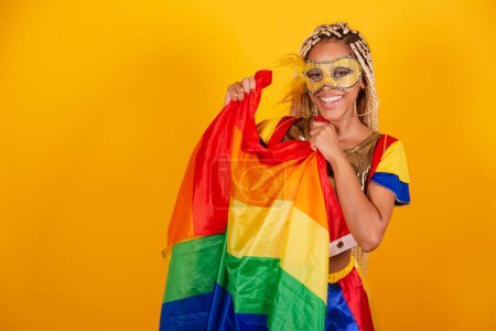 Photo for Beautiful black Brazilian woman, dressed in carnival clothes, mask. yellow background. holding lgbt flag. - Royalty Free Image