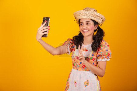 Photo for Beautiful brazilian woman, with festa junina clothes, taking self portrait with smartphone. - Royalty Free Image