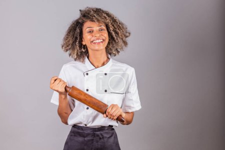Foto de Joven brasileña negra, cocinera, masterchef, vistiendo uniforme de restaurante. soporte de rodillo de madera para preparar pasta, pan y pizza. - Imagen libre de derechos