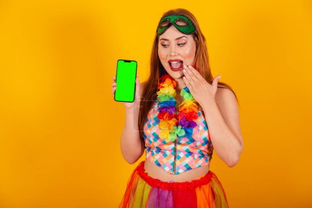 Foto de Pelirroja brasileña, vestida de carnaval, con un collar de flores alrededor del cuello, mostrando un smartphone con pantalla de croma verde. - Imagen libre de derechos
