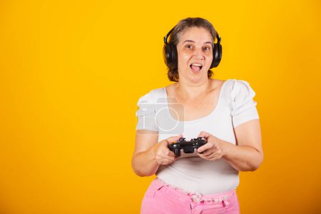Photo for Adult Brazilian woman, mother, holding video game remote control, joystick. Gamer. using headphones, playing online. - Royalty Free Image