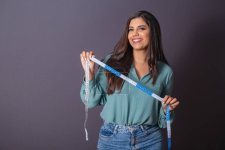 Horizontal photo. Beautiful Brazilian woman, with casual clothes, Jeans and green shirt. nutritionist holding measuring tape.