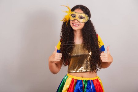 Foto de Jovencita adolescente, brasileña, con ropa frevo, carnaval. máscara, como signo con los dedos. - Imagen libre de derechos