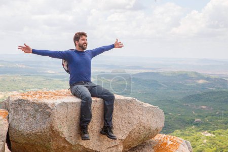 Téléchargez les photos : Homme à bras ouverts assis sur le rocher sur une montagne. Concept d'aventure et de victoire - en image libre de droit