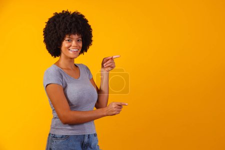 Foto de Mujer afro apuntando en fondo amarillo con espacio para el texto - Imagen libre de derechos