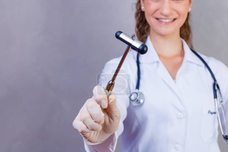Foto de The doctor is holding a neurological hammer on a grey background. The neurologist checks the patient's reflexes with a hammer. Diagnostics, healthcare, and medical care - Imagen libre de derechos