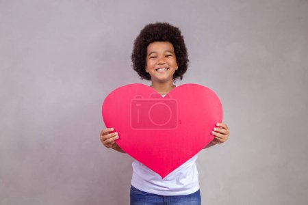 Téléchargez les photos : Mignon afro garçon tenant une grande carte de coeur avec espace pour le texte. - en image libre de droit