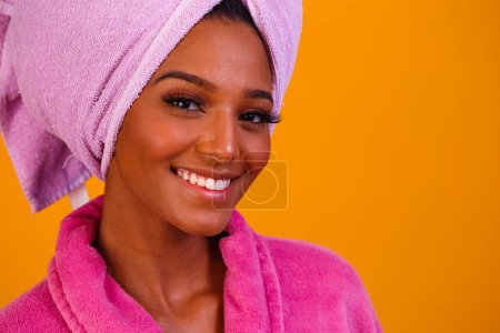Photo for Afro woman with towel on her head and bathrobe after getting out of the bath on yellow background. Bath and care concept - Royalty Free Image