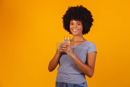 Foto de Joven mujer negra bebiendo agua en fondo amarillo. Chica joven con vaso de agua - Imagen libre de derechos
