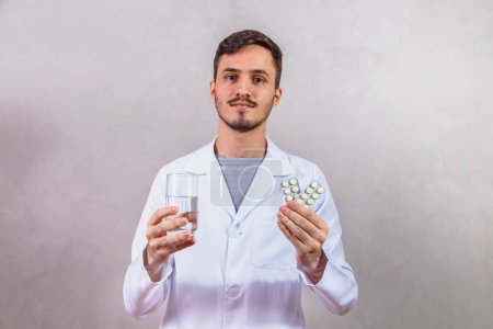 Photo for Male doctor holding glass of water and pills. - Royalty Free Image