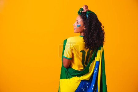 Téléchargez les photos : Un fan brésilien. portant le drapeau brésilien dans un portrait, fan brésilien célébrant le football ou le match de football sur fond jaune. Couleurs du Brazil.World Cup - en image libre de droit