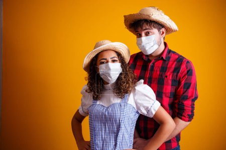 Photo for Couple wearing typical clothes for the Festa Junina (Junina Party) and protection mask to prevent COVID-19. - Royalty Free Image