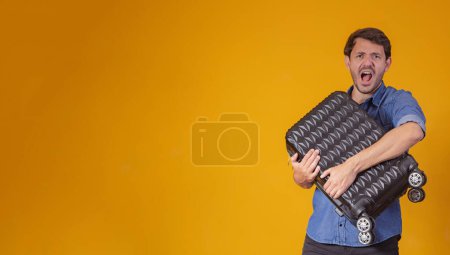 Téléchargez les photos : Homme drôle tenant un sac de voyage lourd. Sur fond jaune - en image libre de droit