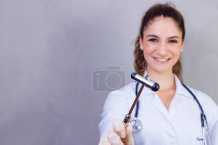 Téléchargez les photos : The doctor is holding a neurological hammer on a grey background. The neurologist checks the patient's reflexes with a hammer. Diagnostics, healthcare, and medical care - en image libre de droit
