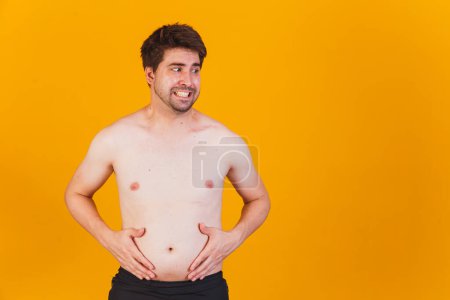 Foto de Hombre tocando su vientre gordo (de cerca). Mano de hombre obeso sosteniendo grasa abdominal excesiva aislada con fondo negro amarillo. reducir el vientre y formar el músculo del estómago sano. - Imagen libre de derechos