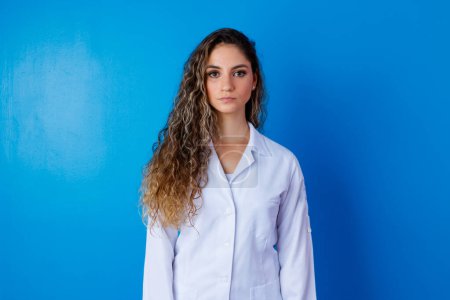 Photo for Young girl in lab coat on blue background with space for text. Woman with white coat. Concept of healthcare professional - Royalty Free Image