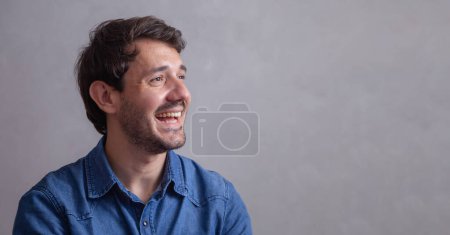 Foto de Chico guapo sobre fondo gris sonriendo mirando una cámara. - Imagen libre de derechos