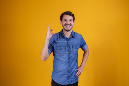 Foto de Retrato de un joven alegre mostrando un gesto aceptable aislado sobre un fondo amarillo. - Imagen libre de derechos