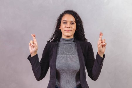 Téléchargez les photos : Jeune femme avec les doigts croisés et regardant loin sur fond gris - en image libre de droit