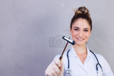 Téléchargez les photos : Le médecin tient un marteau neurologique sur un fond gris. Le neurologue vérifie les réflexes du patient avec un marteau. Diagnostic, soins de santé et soins médicaux - en image libre de droit