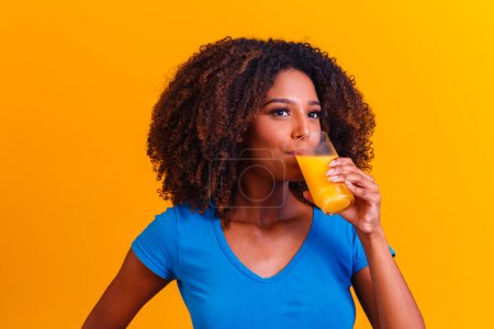 Téléchargez les photos : Femme afro-américaine buvant du jus d'orange en fond jaune - en image libre de droit