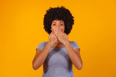 Foto de Mujer negra sobre fondo amarillo con la mano en la boca, concepto de abuso, feminicidio, racismo y prejuicio - Imagen libre de derechos