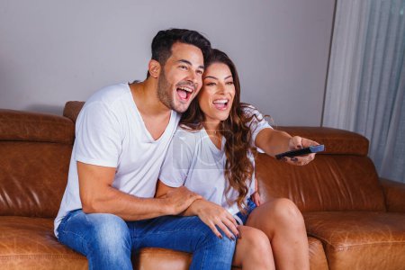 Téléchargez les photos : Couple Valentine avec télécommande regarder la télévision sur le canapé confortable - en image libre de droit