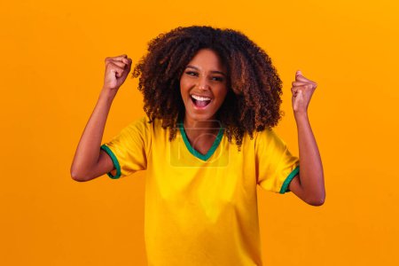 Foto de Apoyador brasileño. Aficionada brasileña celebrando en el fútbol o partido de fútbol sobre fondo amarillo. Brasil colores. - Imagen libre de derechos