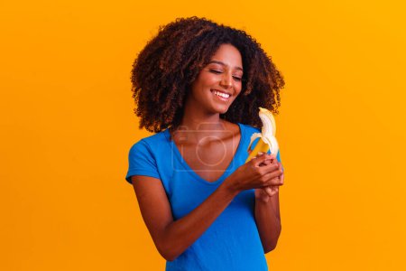 Téléchargez les photos : Jeune fille afro manger de la banane. Concept de santé. Une alimentation saine - en image libre de droit
