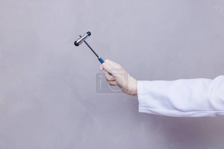 Téléchargez les photos : Le médecin tient un marteau neurologique sur un fond gris. Le neurologue vérifie les réflexes du patient avec un marteau. Diagnostic, soins de santé et soins médicaux - en image libre de droit