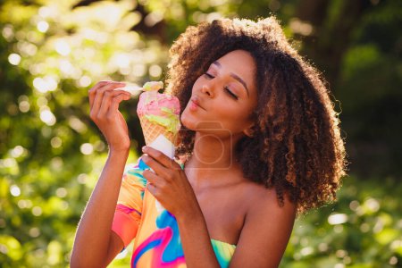 Téléchargez les photos : Happy afro femme manger de la crème glacée dans le parc. - en image libre de droit