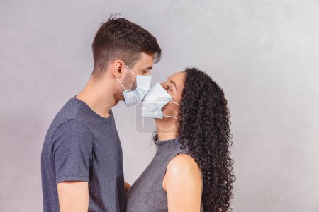 Photo for Young millennials couple wearing protective face masks and kissing each other, virus spread prevention and people concept. Valentine couple with mask. Quarantine - Royalty Free Image