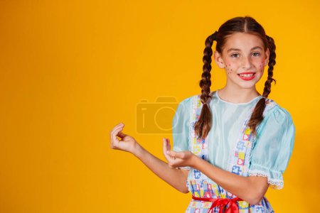Photo for Child in typical clothes of famous Brazilian party called Festa Junina in celebration of So Joo. Beautiful girl on yellow background. - Royalty Free Image