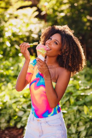 Téléchargez les photos : Happy afro femme manger de la crème glacée dans le parc. - en image libre de droit