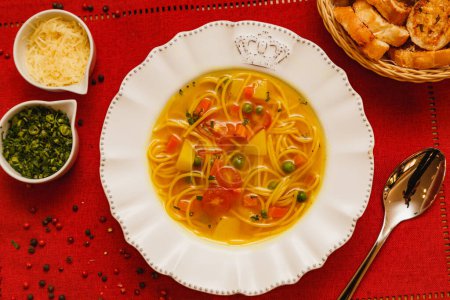 Téléchargez les photos : Délicieuse soupe aux nouilles aux légumes, soupe aux nouilles aux légumes, sur fond de bois, fond de tissu rouge, avec pain grillé, persil et parmesan, plats d'hiver brésiliens, cuisine gastronomique - en image libre de droit