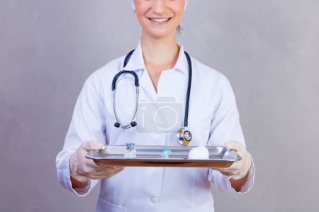 Foto de Enfermera sosteniendo bandeja con medicinas sobre fondo gris. Médicos sobre fondo gris. Vacuna y medicamentos. Concepto de salud y atención - Imagen libre de derechos