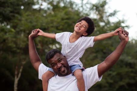 Foto de Afro chico con su padre en el parque en su cuello - Imagen libre de derechos