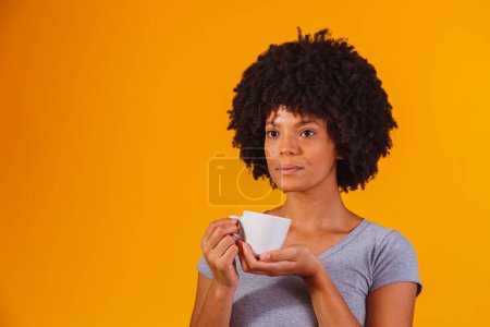 Téléchargez les photos : Afro femme prenant le thé sur fond jaune - en image libre de droit