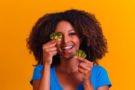 Photo for Happy afro woman eating brocolis. woman with brocolis on yellow background. healthy eating concept - Royalty Free Image