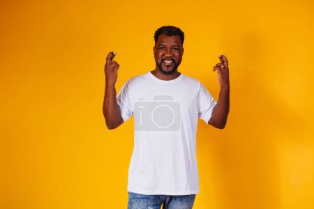 Photo for Afro man with fingers crossed on yellow background - Royalty Free Image
