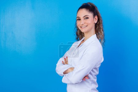 Photo for Portrait of confident with toothy beaming smile qualified experienced clever intelligent doctor wearing white formal wear she is standing with crossed folded arms, isolated on blue background - Royalty Free Image