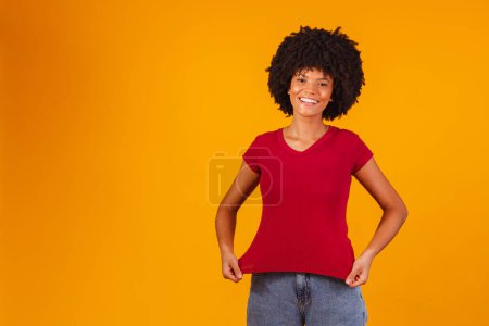 Téléchargez les photos : Afro femme pointant vers le t-shirt avec espace pour le texte. - en image libre de droit