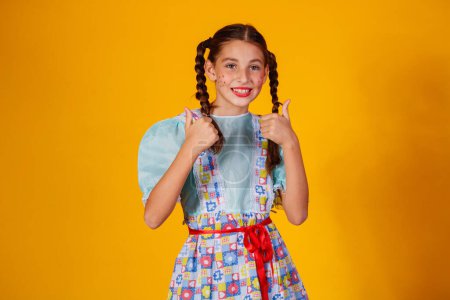 Téléchargez les photos : Enfant en vêtements typiques de la célèbre fête brésilienne appelée Festa Junina pour célébrer So Joo. Belle fille sur fond jaune. - en image libre de droit