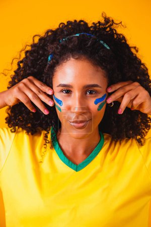 Téléchargez les photos : Un fan brésilien. utilisant la peinture comme maquillage, ventilateur brésilien célébrant le football ou le match de football sur fond jaune. Couleurs du Brésil. - en image libre de droit